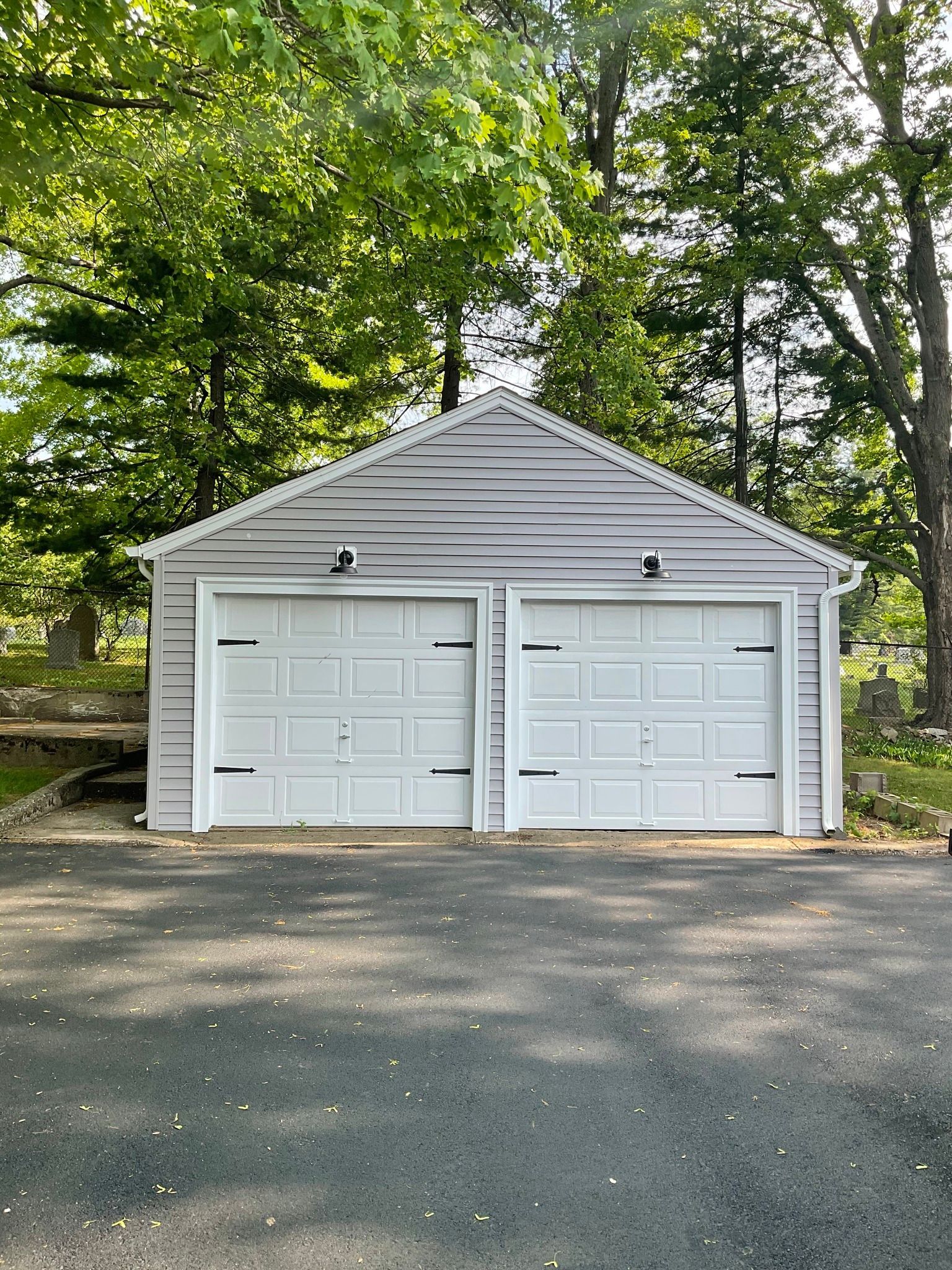A garage with two white garage doors is surrounded by trees.