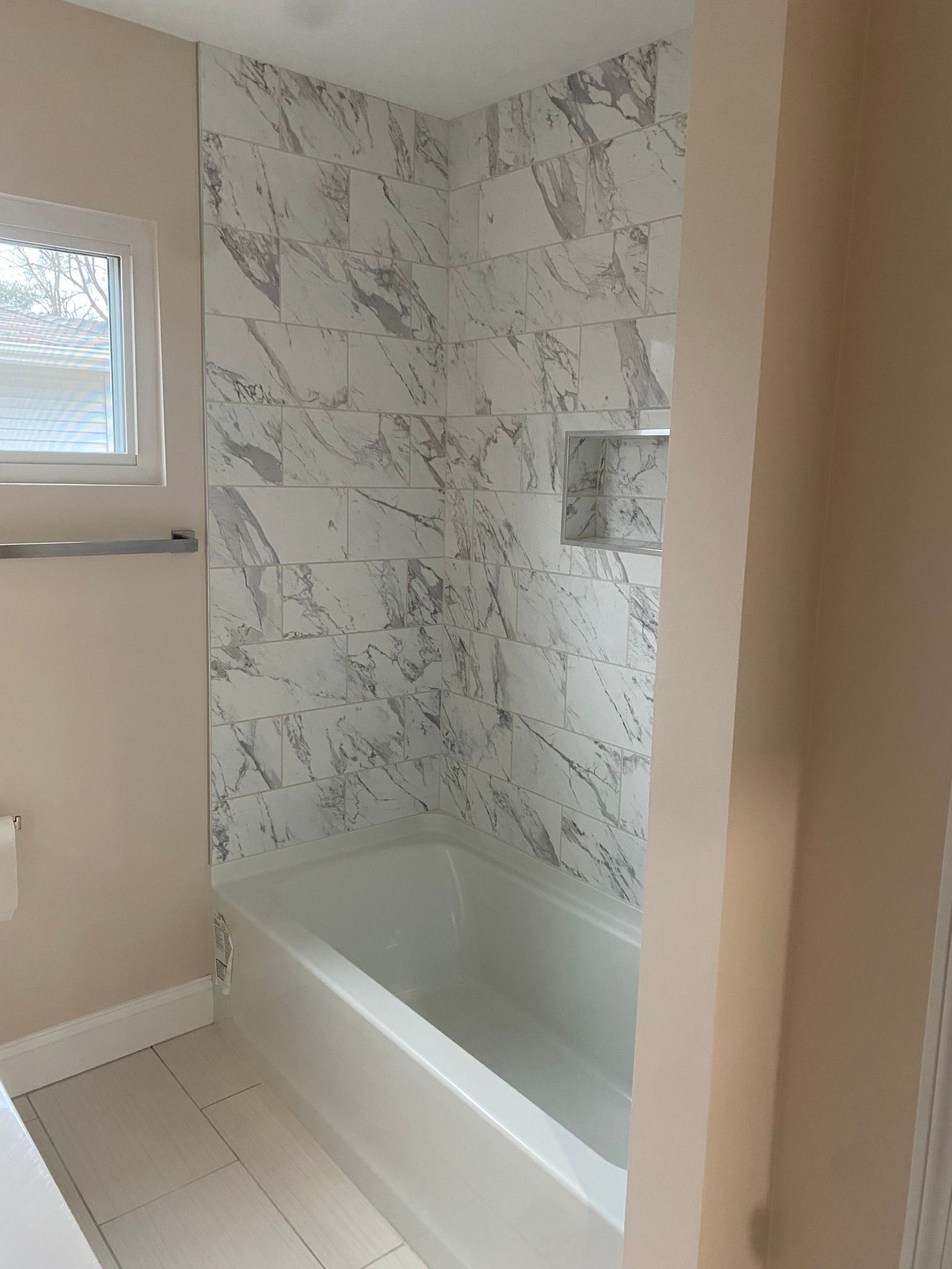 There is a bathtub in the bathroom with marble tiles on the wall.