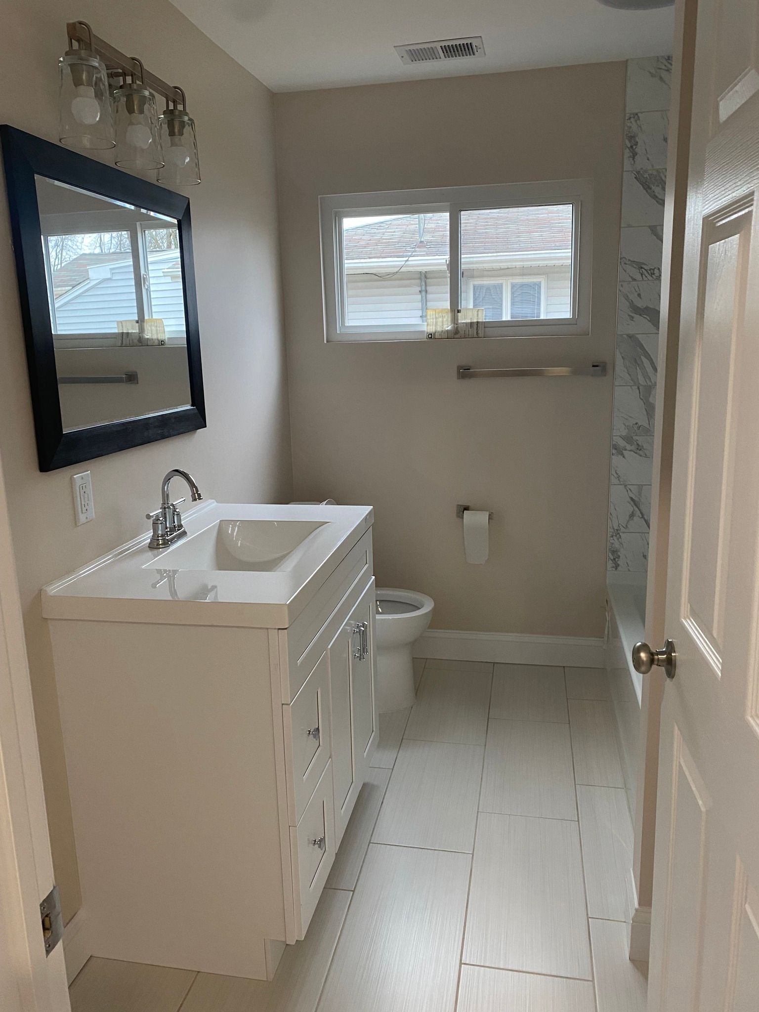 A bathroom with a sink , toilet , mirror and window.
