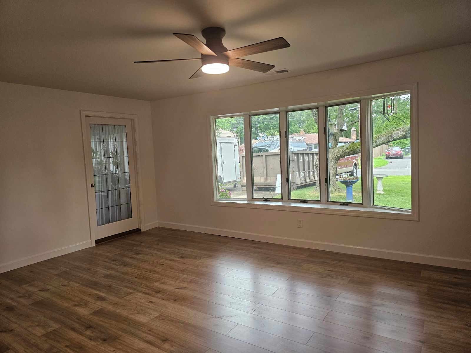 An empty living room with a ceiling fan and lots of windows.