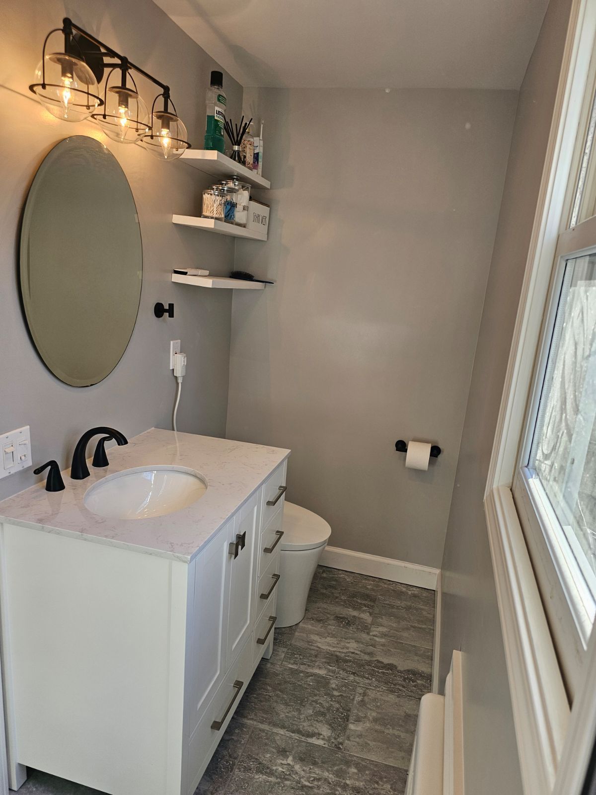 A bathroom with a sink , toilet , mirror and window.