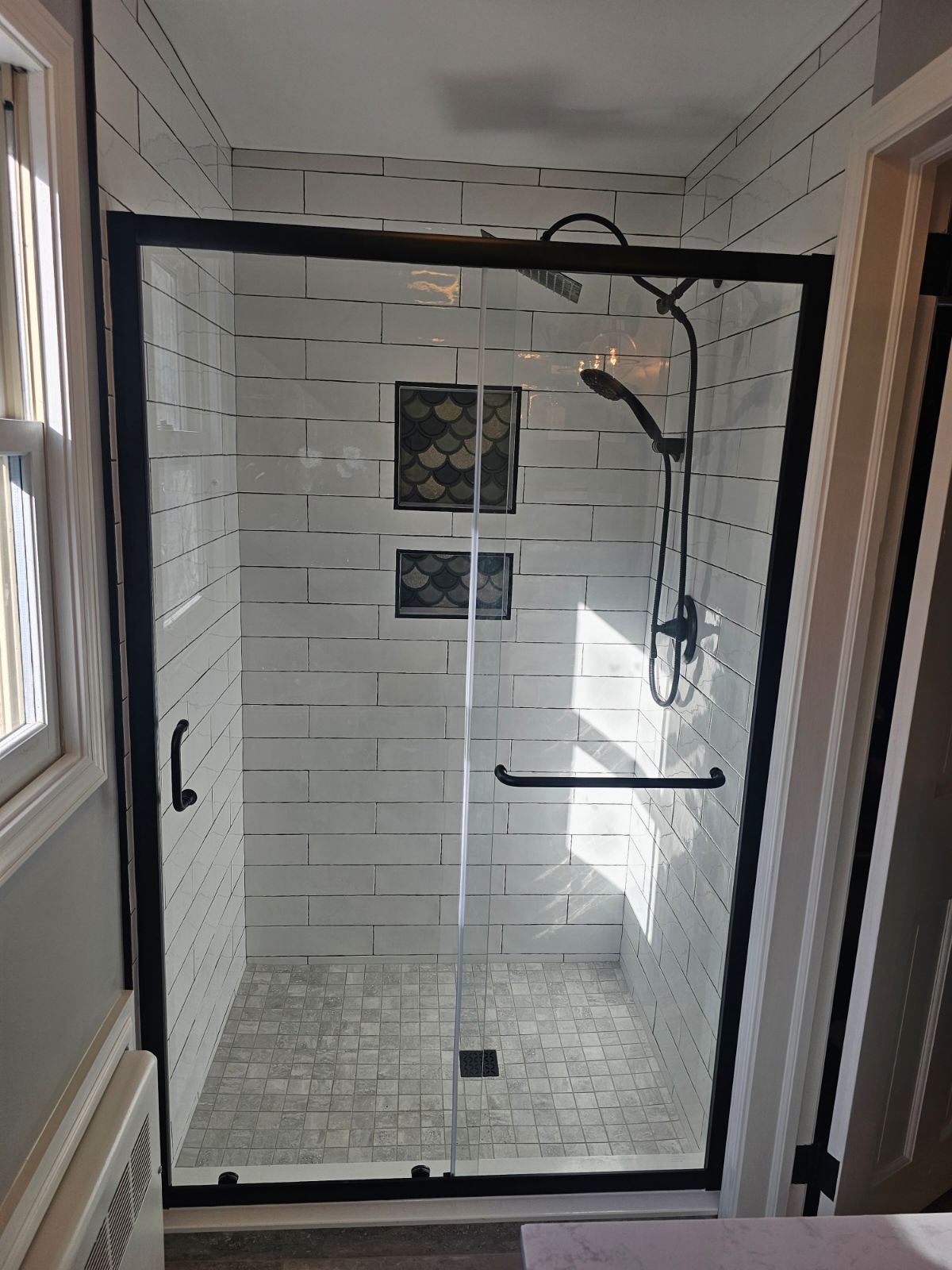 A bathroom with white tiles and a black shower door