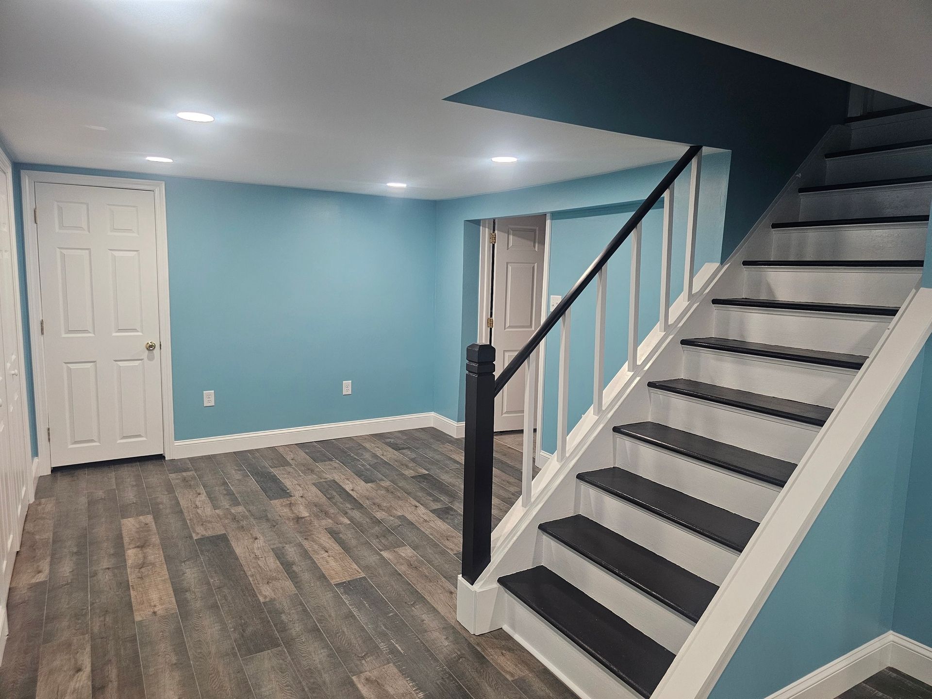 A basement with blue walls and black and white stairs.