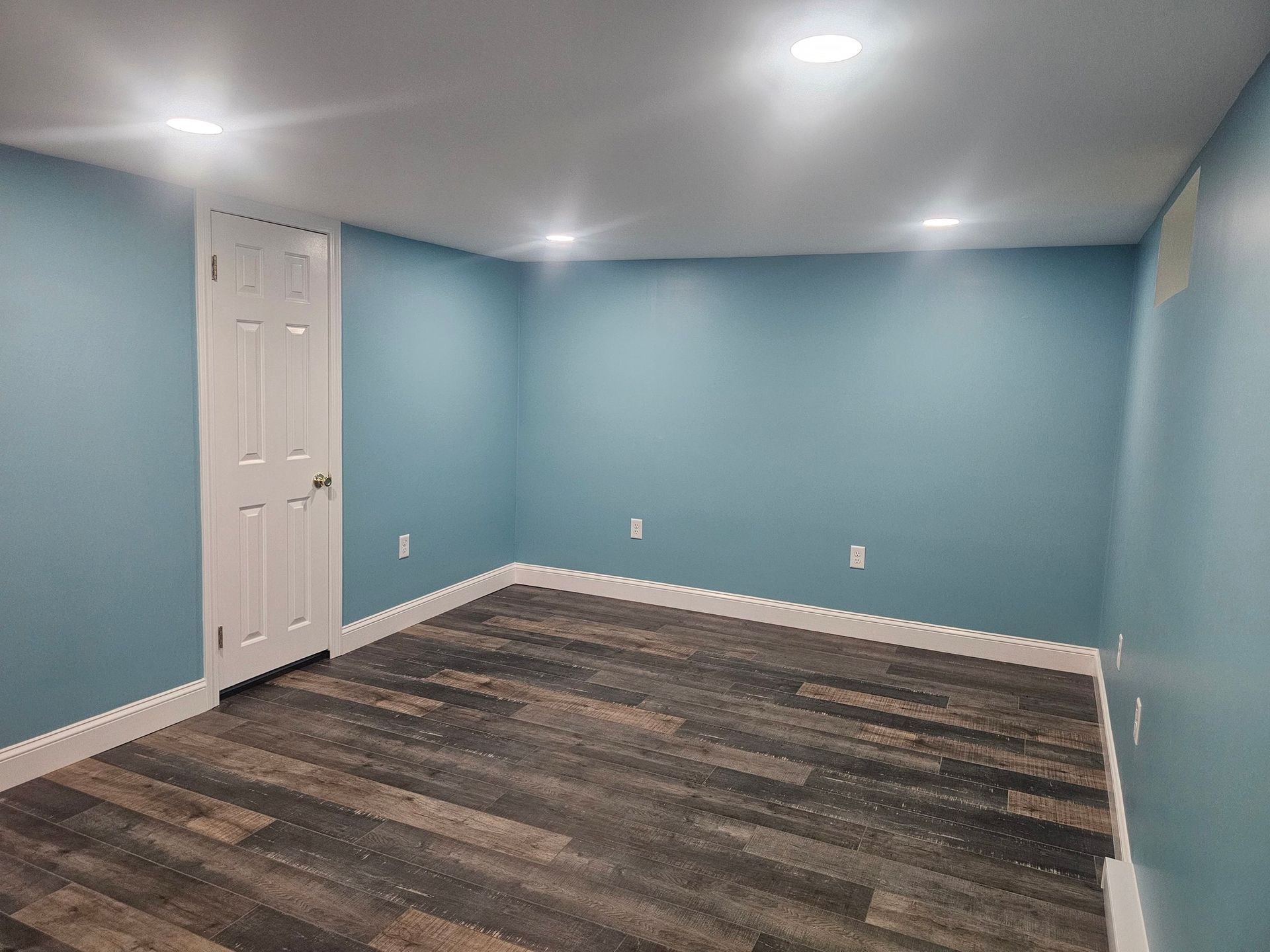 An empty basement with blue walls and wooden floors.