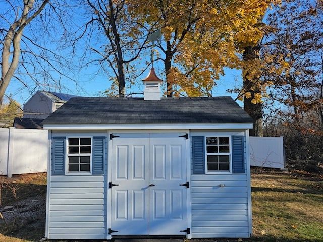 A white shed with blue shutters and a chimney on top of it.