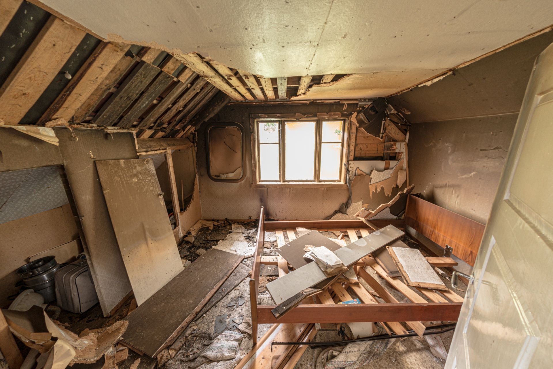 Dilapidated room with collapsed ceiling, broken bed frame, debris, and a window letting in light