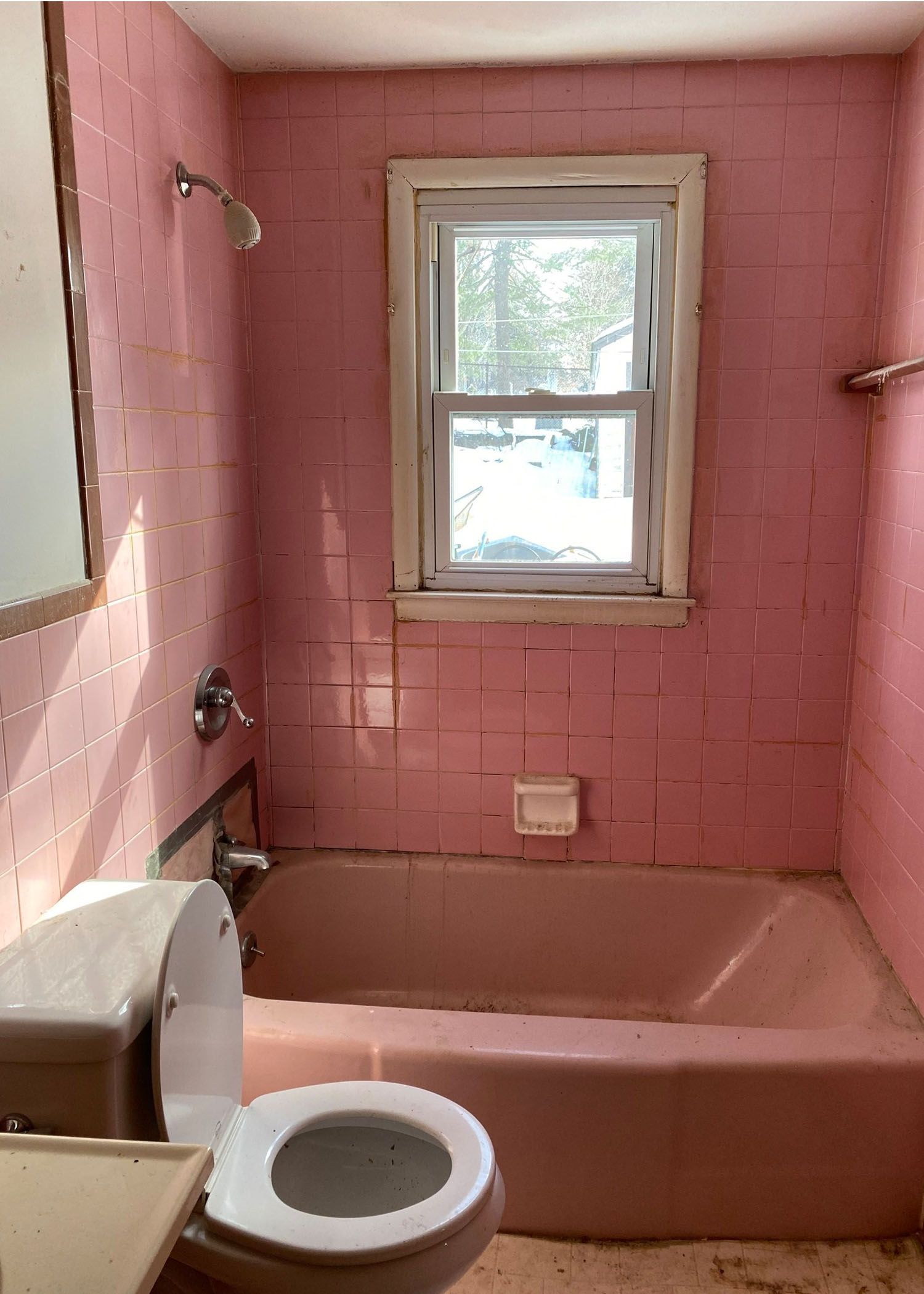 A bathroom with pink tiles , a toilet , a tub and a window.