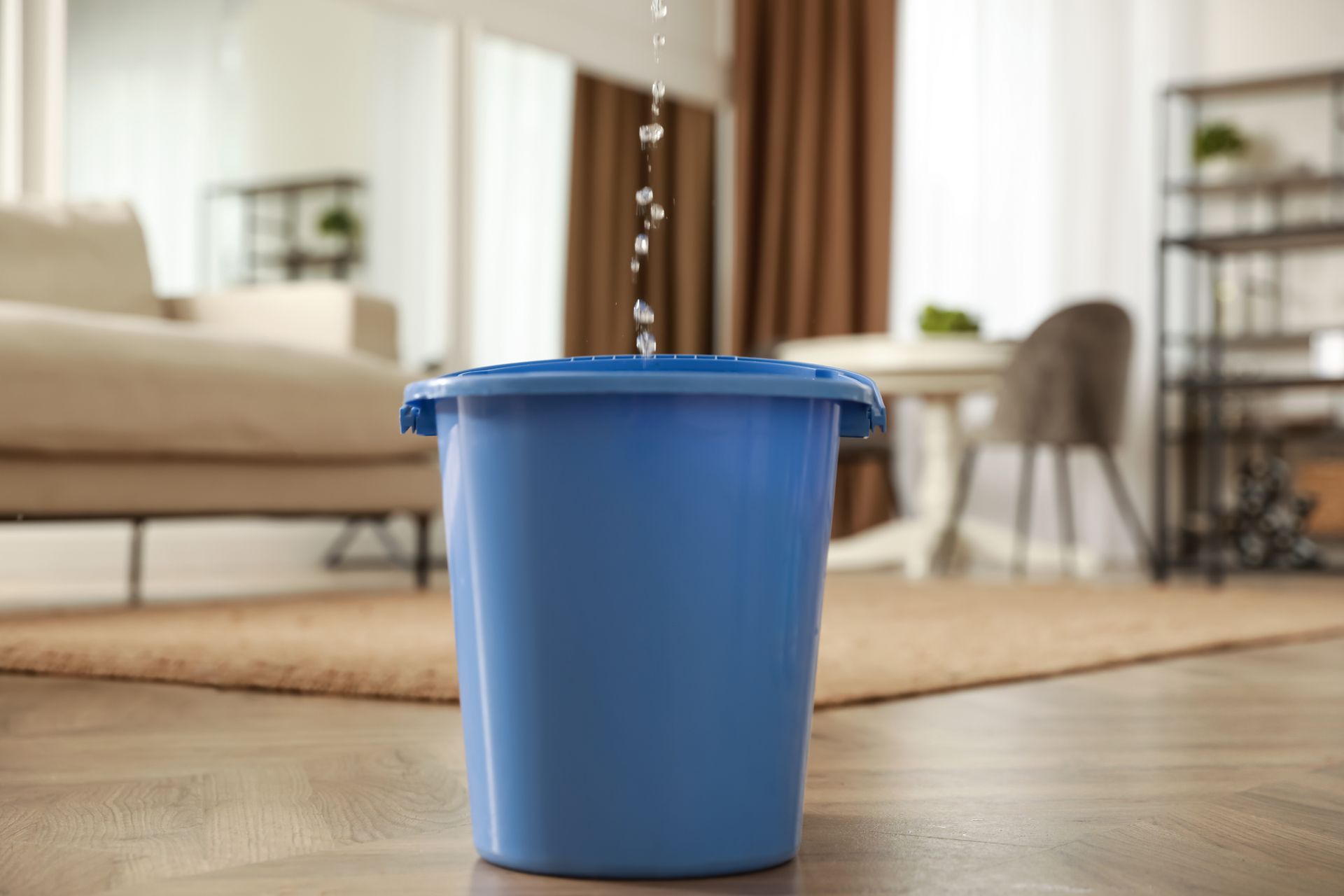 Blue bucket on a living room floor with water pouring into it from above