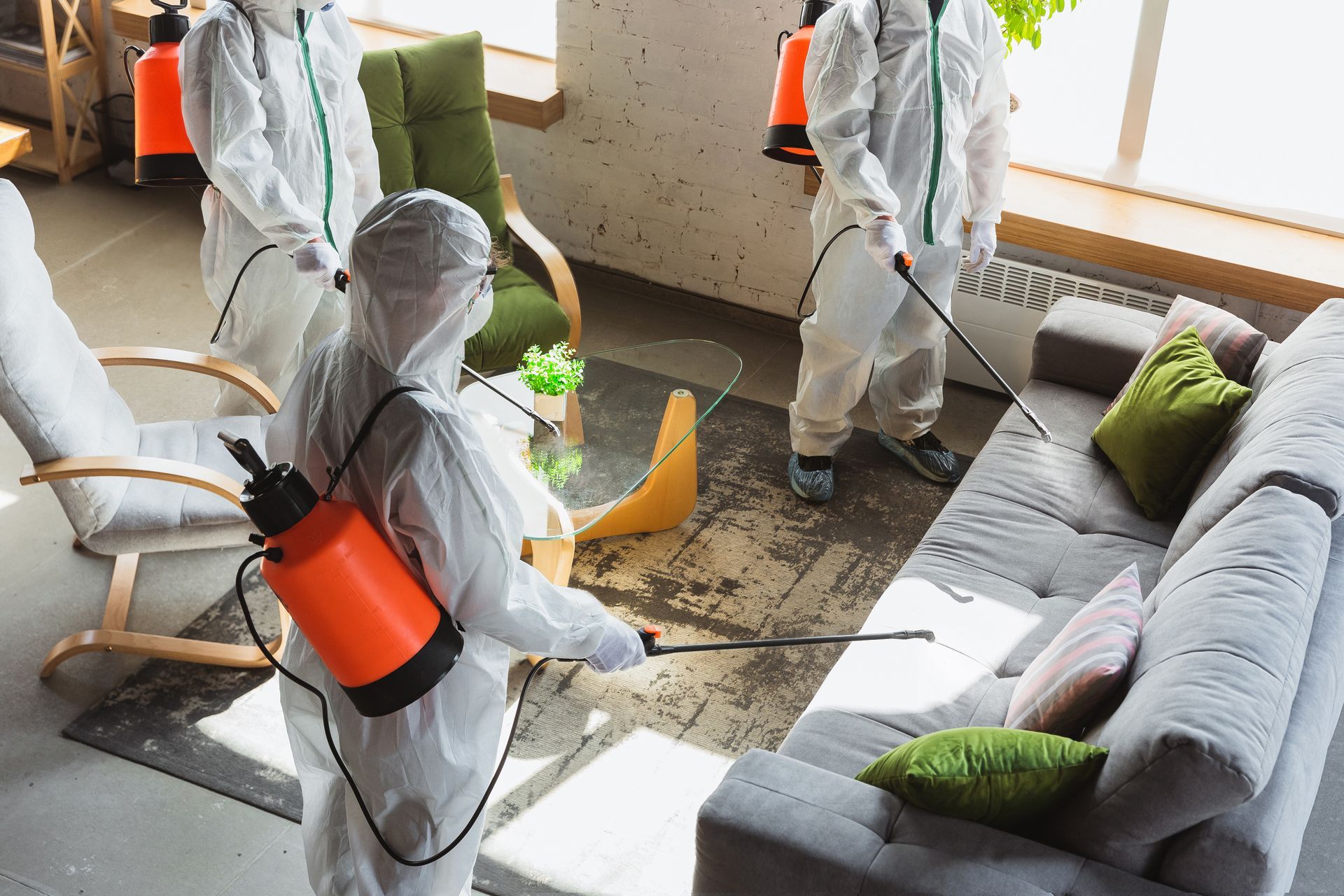 People in hazmat suits spraying a living room with disinfectant.