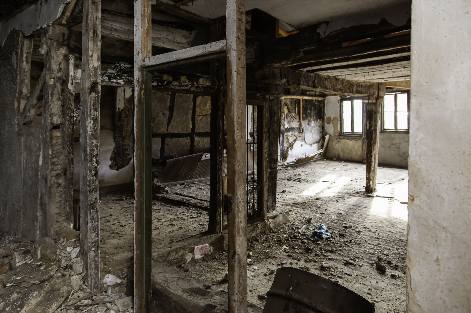 Interior of a heavily damaged building, walls and supports charred and exposed, debris on the floor, windows visible in the background.