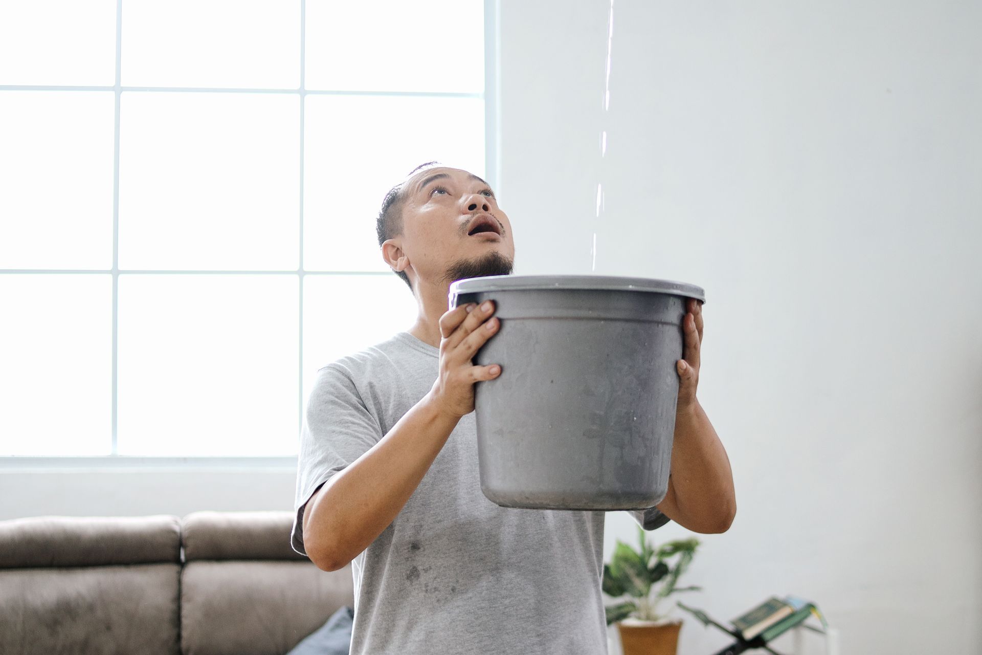 Man holding a bucket to catch water leaking from the ceiling in a living room.