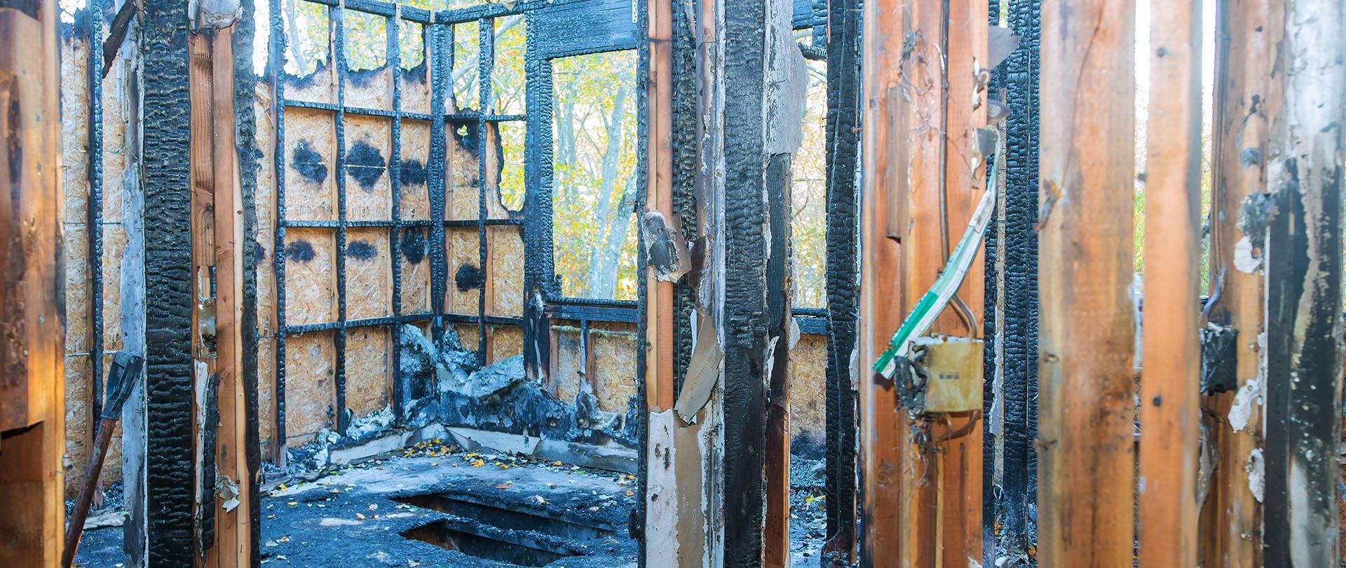 Interior of a burned wooden structure, charred wood and blackened interior. Light from outside visible through a window.