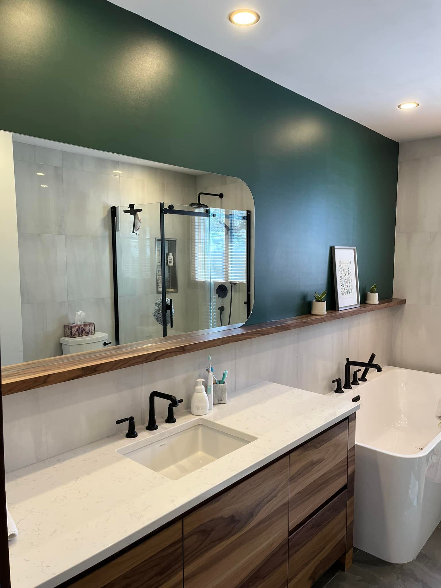 Salle de bains moderne avec meuble-lavabo en bois, comptoir blanc, mur d'accent vert et grand miroir.