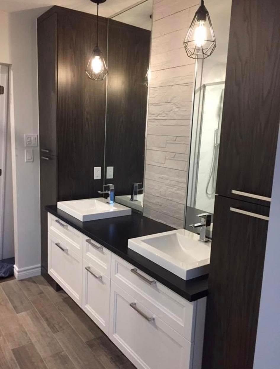 Salle de bains moderne avec double vasque, meubles foncés, lavabos blancs et deux suspensions lumineuses.