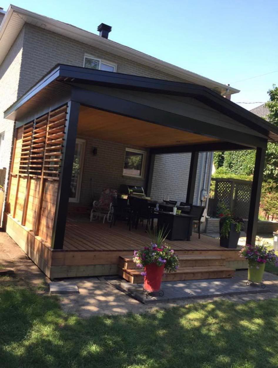 Terrasse arrière avec pergola à structure sombre, brise-vue en lattes de bois et mobilier de jardin. Pelouse verte à l'avant.