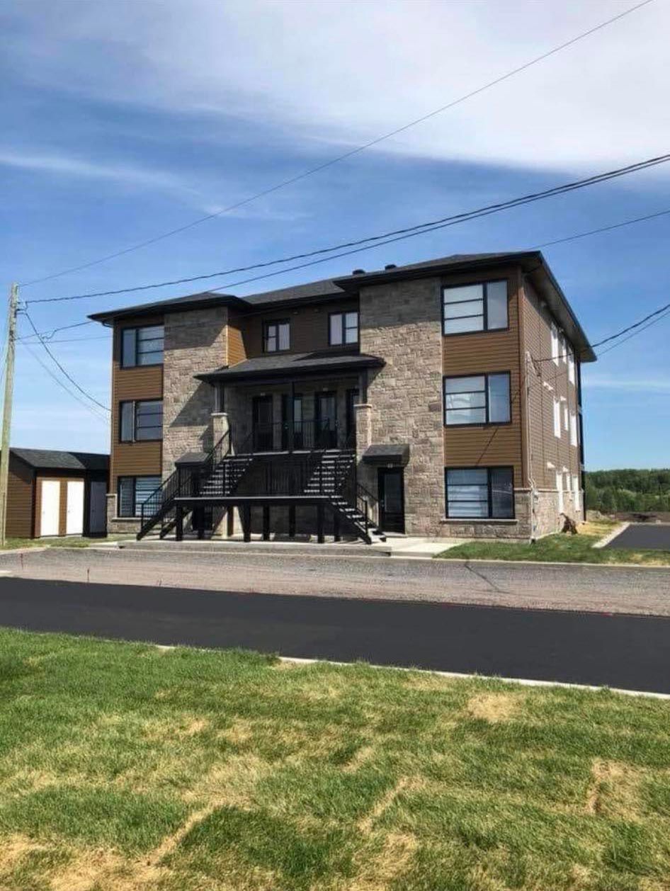 Immeuble d'appartements de deux étages avec revêtement en briques et en bois, balcons noirs et ciel bleu clair.