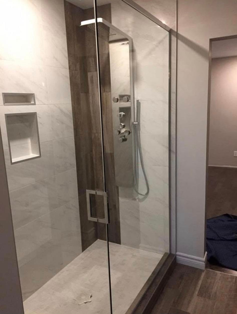 Douche moderne avec porte en verre, murs carrelés et pommeau de douche effet pluie.