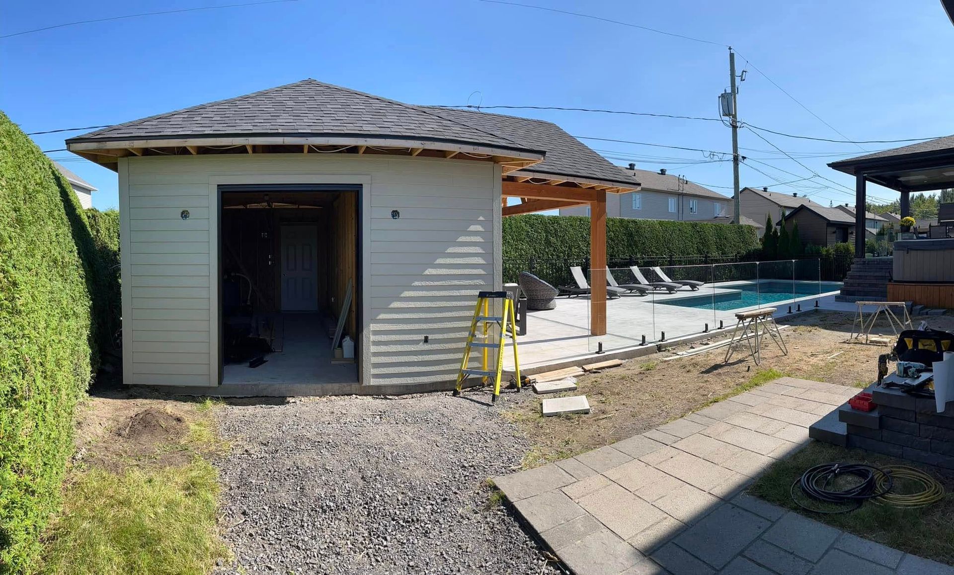 Jardin avec un bâtiment clair, une piscine et des travaux de construction en cours par une journée ensoleillée.