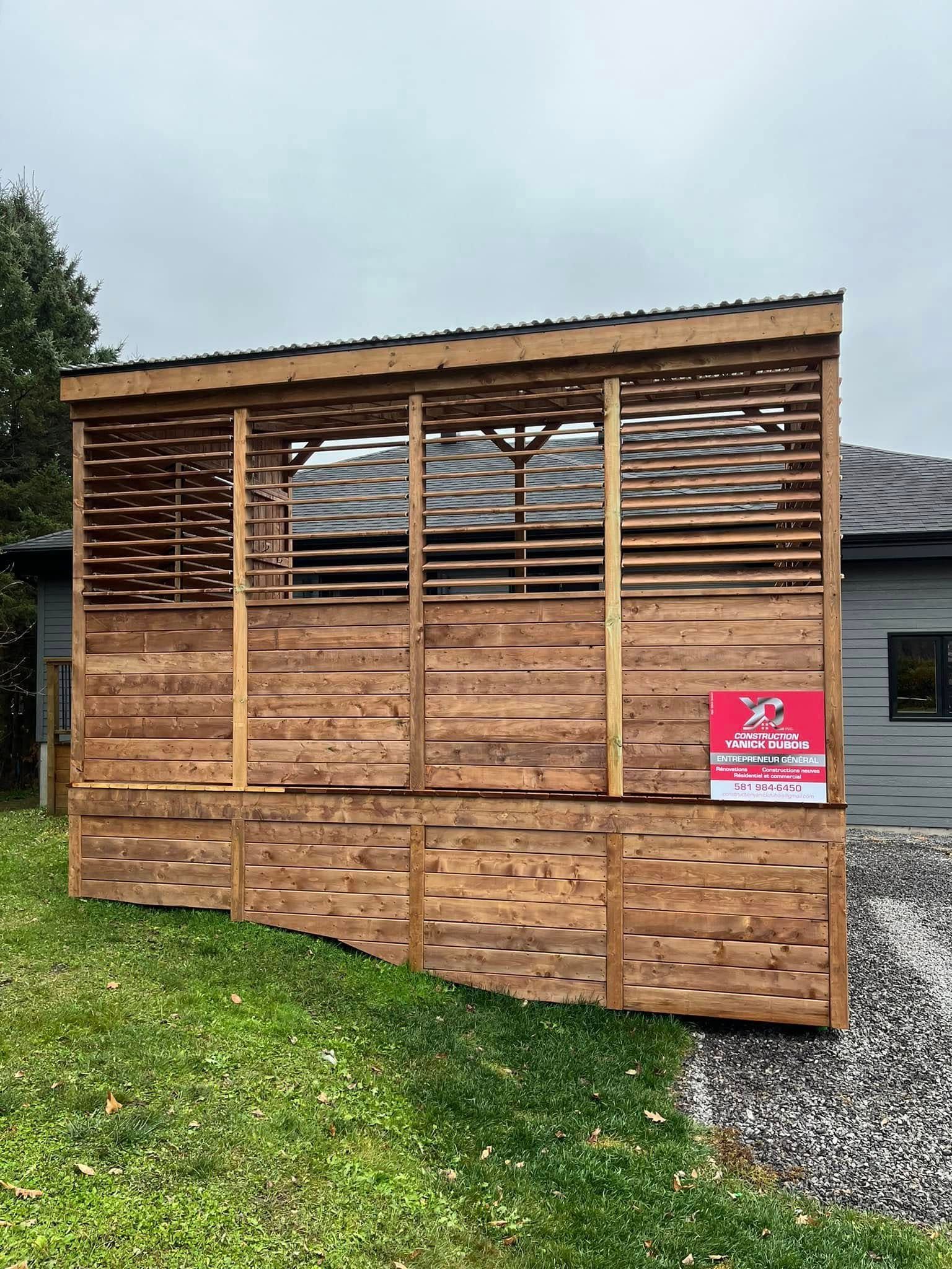 Structure extérieure en bois avec parois à claire-voie, toit en pente et panneau latéral, dans un jardin gazonné.