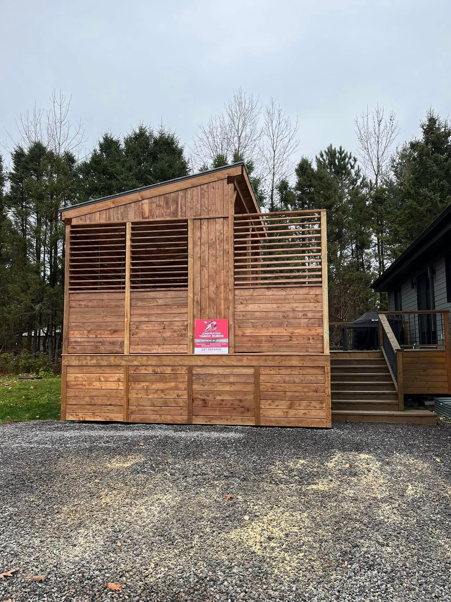 Structure extérieure en bois aux parois à claire-voie, jouxtant une maison avec escalier.
