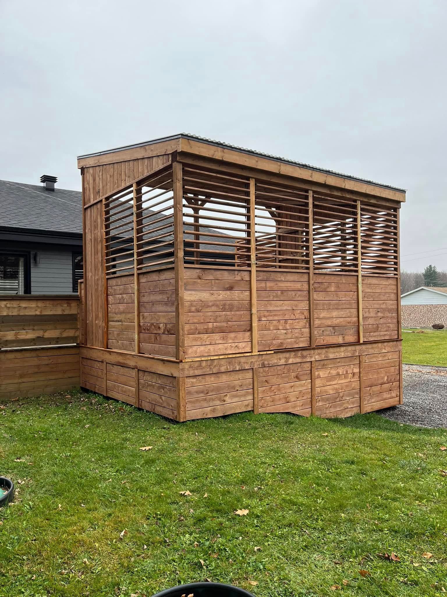 Gazebo extérieur en bois avec parois et toit en treillis, sur une pelouse.