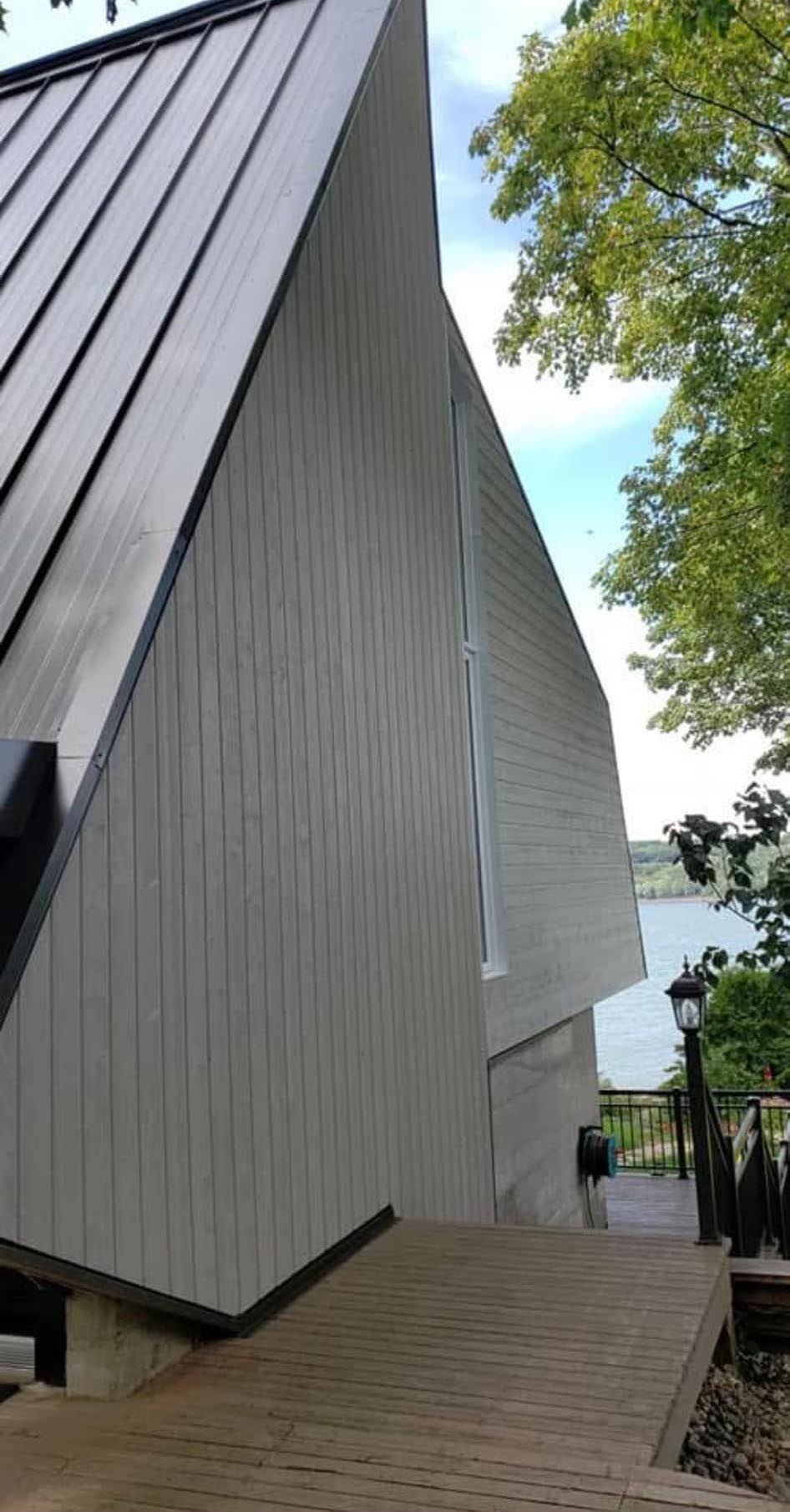 Bâtiment angulaire aux façades grises et au toit noir ; une passerelle en bois mène à l'entrée située près d'un lac.