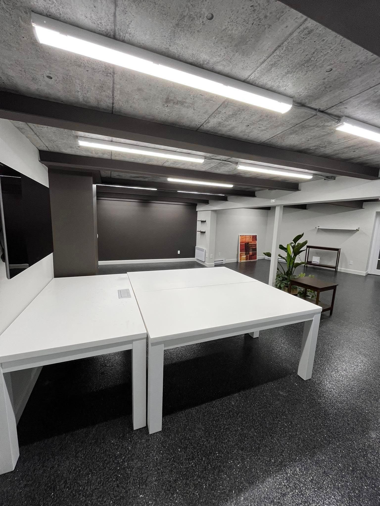 Intérieur de bureau avec bureaux blancs, sol foncé et palette de couleurs neutres.