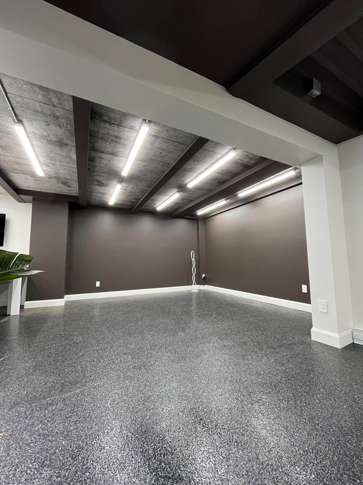 Pièce vide aux murs gris foncé, au sol moucheté et à l'éclairage fluorescent.