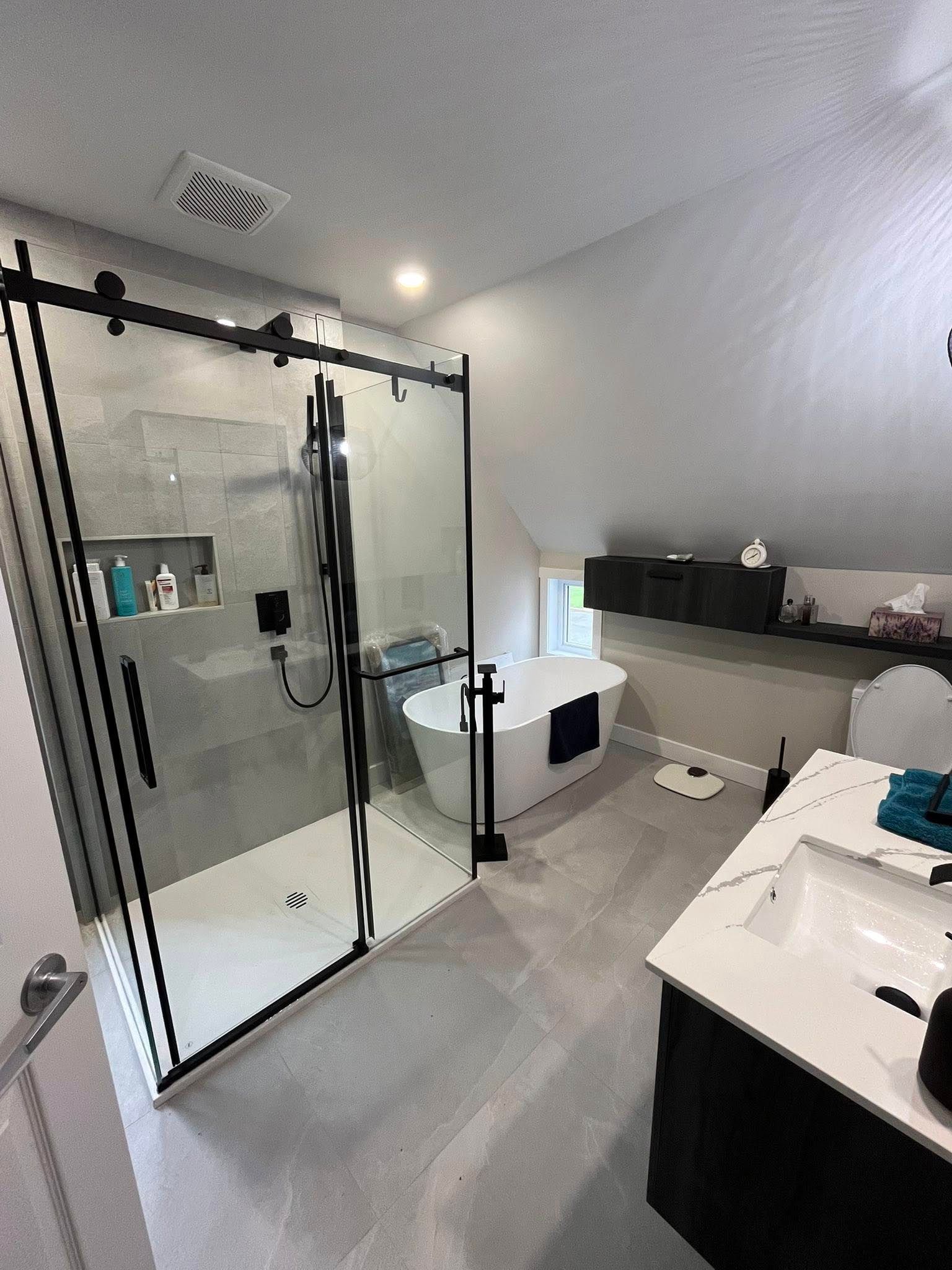 Salle de bains moderne avec douche en verre, baignoire îlot, meuble-lavabo et plafond mansardé.