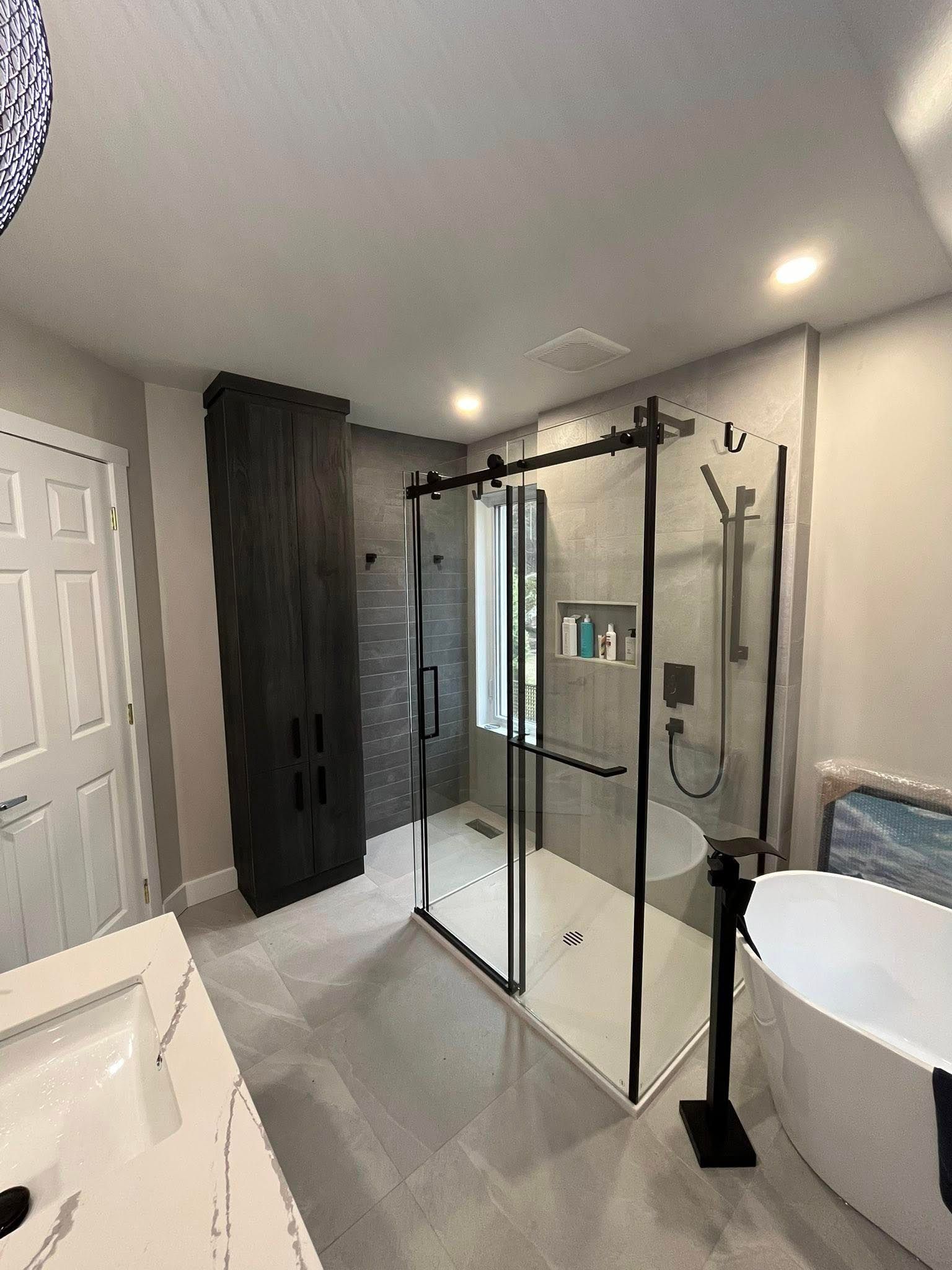 Salle de bains moderne avec douche en verre, baignoire et meuble de rangement en bois foncé.