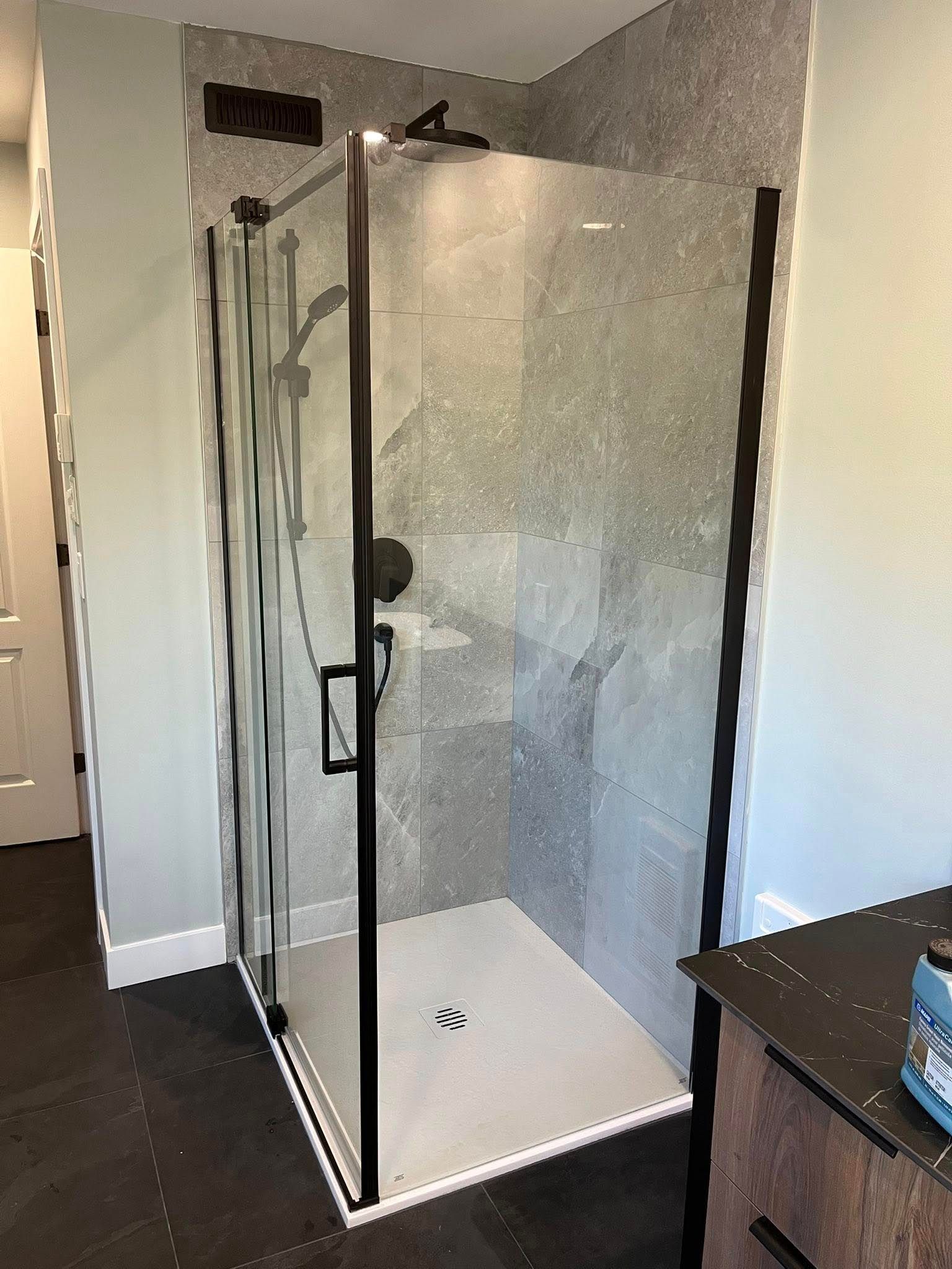 Douche moderne avec carrelage gris, cadre noir, porte en verre et receveur de douche blanc.