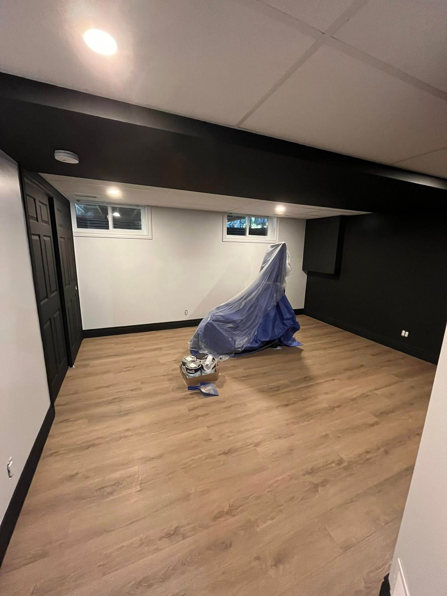 Pièce au sous-sol avec des touches de noir, des murs noirs, un parquet et un objet recouvert au centre.