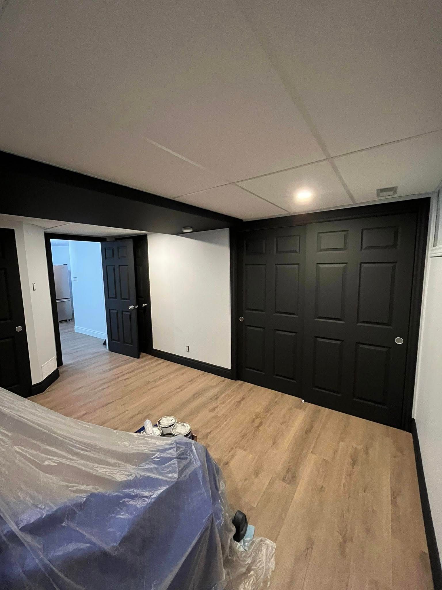 Pièce avec parquet clair, moulures noires, murs blancs et portes de placard noires.