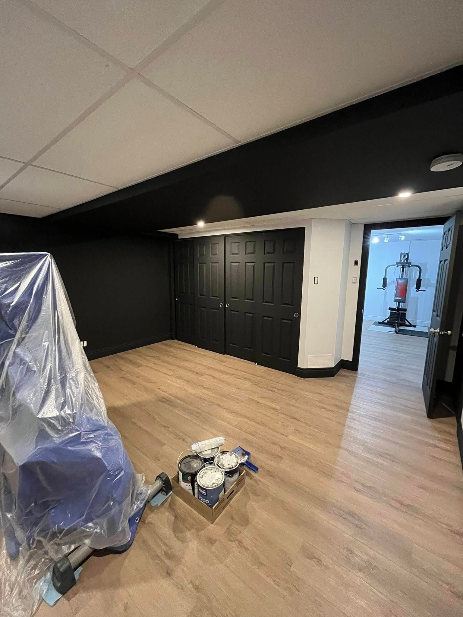 Pièce au sous-sol avec murs noirs, plafond blanc, parquet et une porte donnant sur une salle de sport.