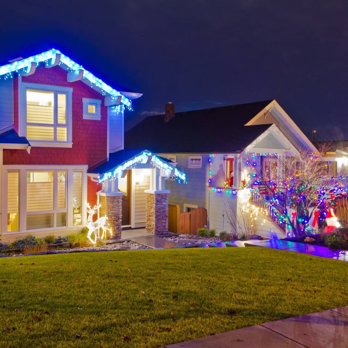 Houses decorated with blue, red, and multicolored Christmas lights at night.