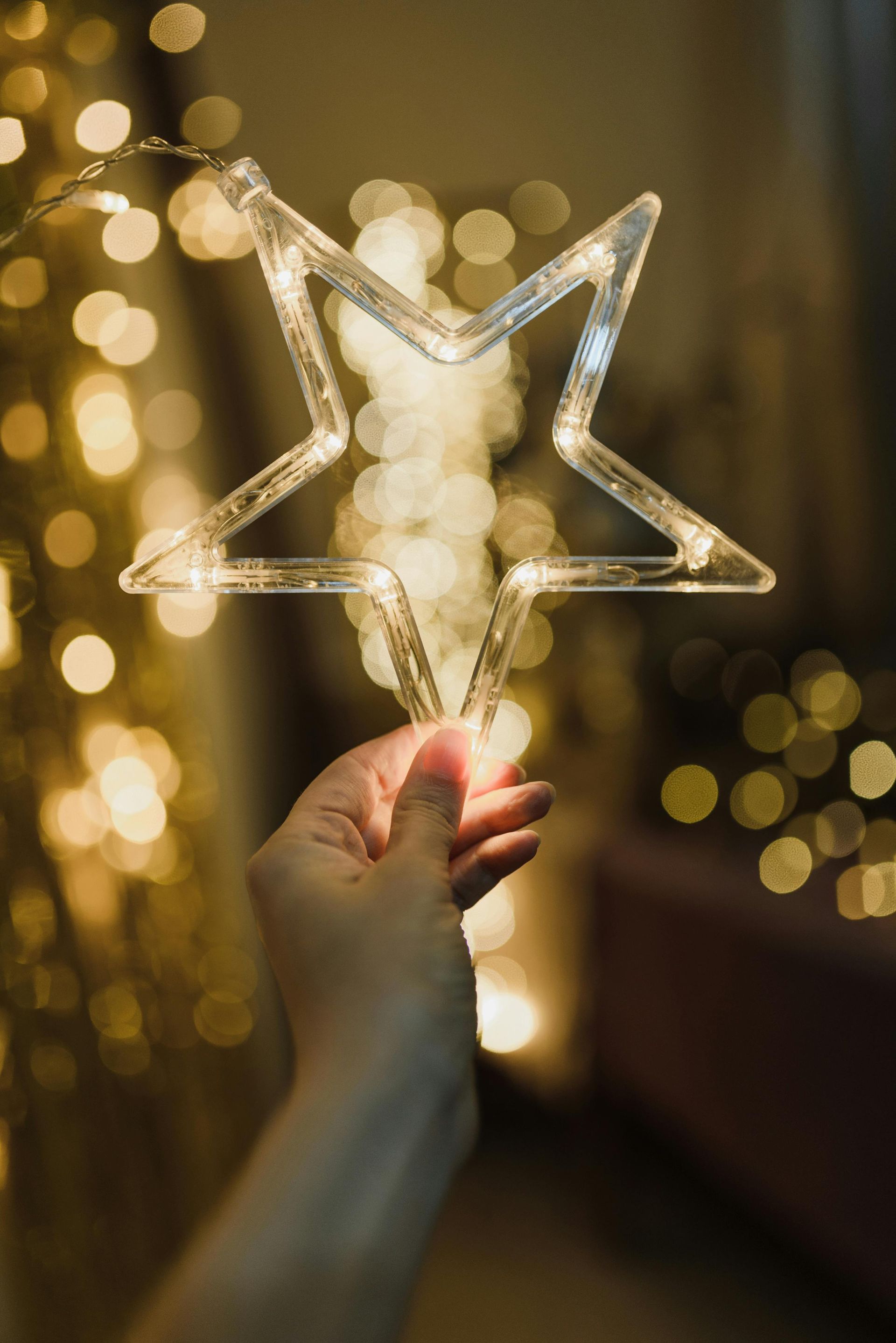Hand holding a glowing star-shaped light with a warm, blurred background of bokeh lights.