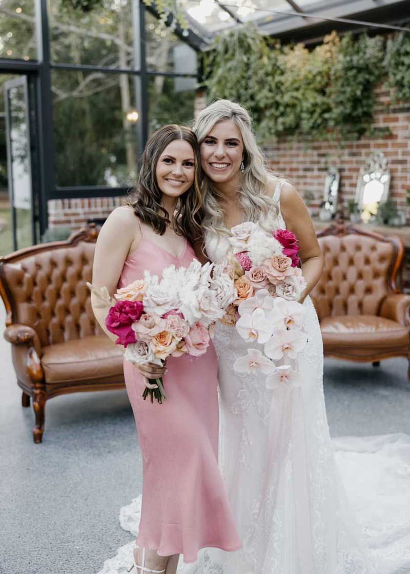A bride and her bridesmaid are posing for a picture while holding bouquets of flowers.