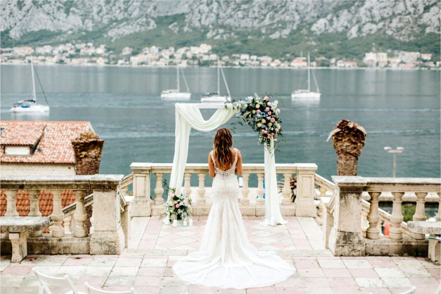 A bride in a wedding dress is standing on a balcony overlooking the ocean.