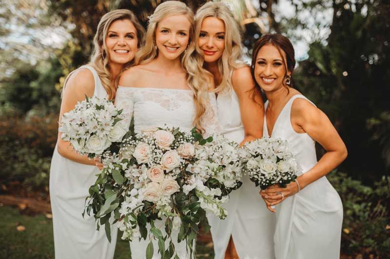 A bride and her bridesmaids are posing for a picture while holding bouquets of flowers.