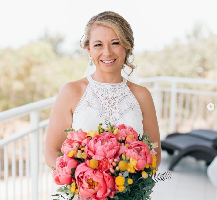 A bride in a white dress is holding a bouquet of pink and yellow flowers.