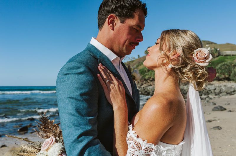 A bride and groom are kissing on the beach.