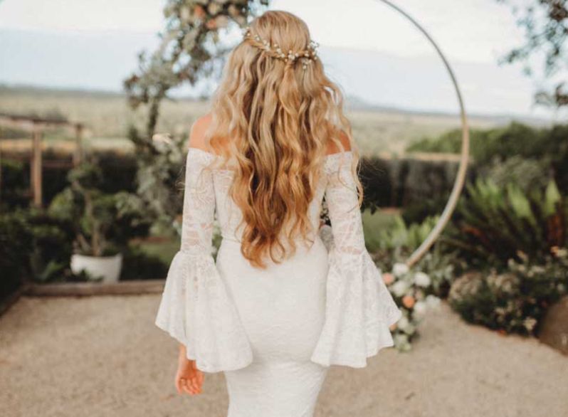 The bride is wearing a white dress with bell sleeves and a flower crown on her head.