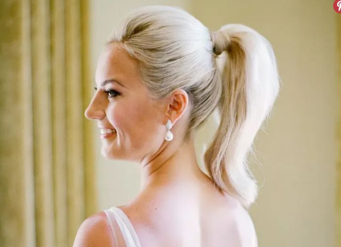 A woman in a white dress is wearing a ponytail and earrings.