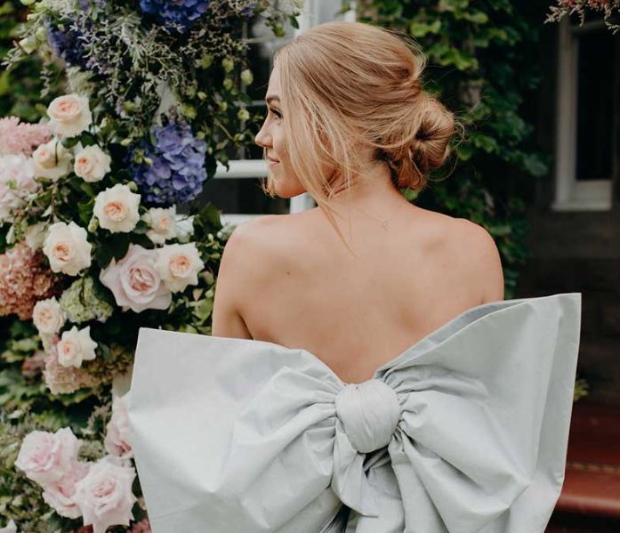 A woman is wearing a white dress with a large bow on the back.