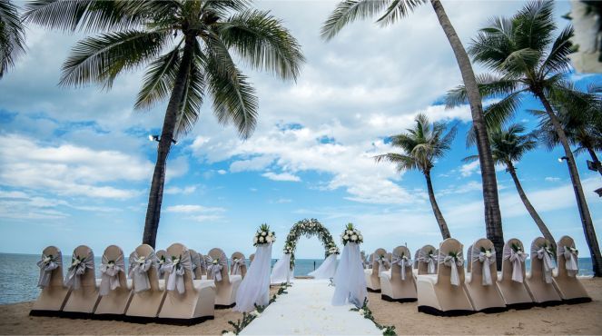 A bride and groom are standing on a beach holding hands.