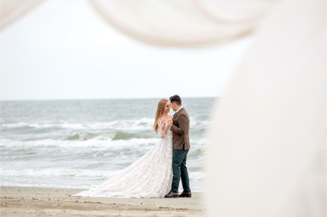 A bride and groom are kissing on the beach.