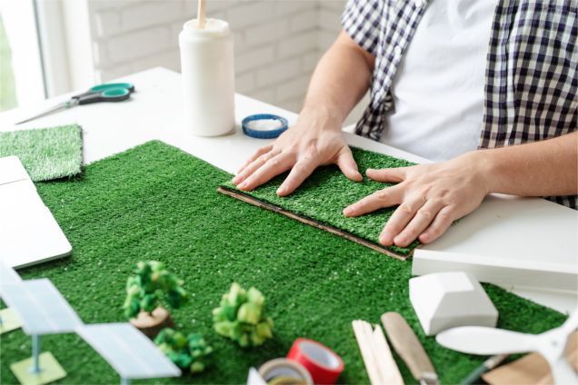 A man is sitting at a table making a model of a grassy field.