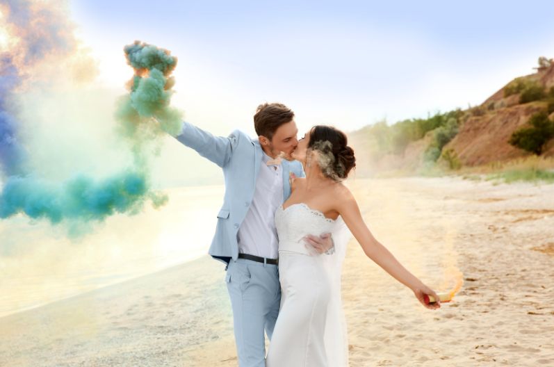 A bride and groom are posing for a picture on the beach.