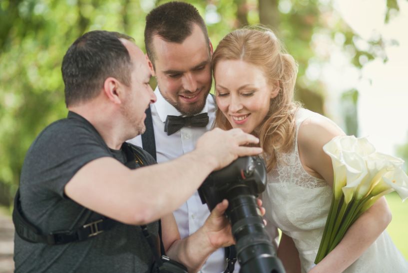 A man is taking a picture of a bride and groom with a camera.