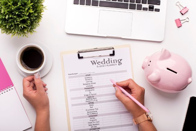 A woman is writing on a clipboard next to a piggy bank and a laptop.